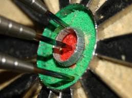 Red dot on the wall; Close of of darts in bullseye